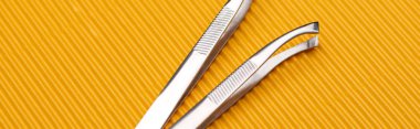 stainless steel tweezers on yellow textured background, panoramic shot clipart