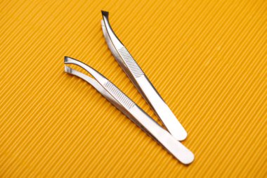stainless steel tweezers on yellow textured background clipart