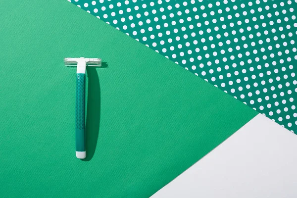 top view of green disposable razor on green dotted background