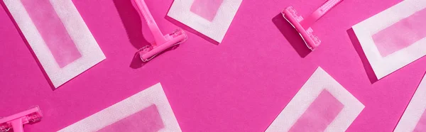 top view of disposable razors and wax depilation stripes on pink background, panoramic shot