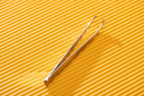 stainless steel tweezers on yellow textured background