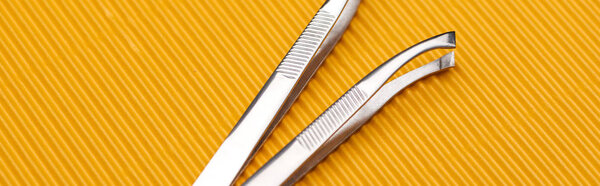 stainless steel tweezers on yellow textured background, panoramic shot