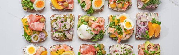 panoramic shot of traditional danish smorrebrod sandwiches on white marble surface 