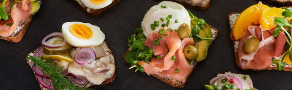 panoramic shot of rye bread with prepared danish smorrebrod sandwiches on grey surface 