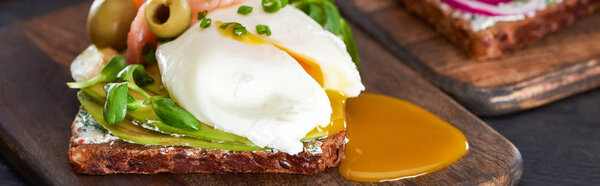 panoramic shot of smorrebrod sandwich with poached egg on wooden cutting board 