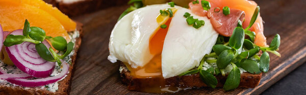 panoramic shot of fresh smorrebrod sandwich with poached egg on wooden cutting board 