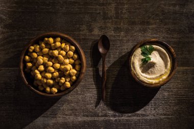 Tahta kırsal masada kaşığın yanındaki kaselerde lezzetli humus ve nohut manzarası.