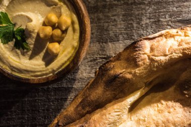 Tahta kırsal masada taze pişmiş pidenin yanında bezelyeli leziz humus manzarası.