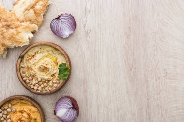 Lezzetli humus, taze pişmiş pidenin yanında nohut, bej ahşap masada kırmızı soğan.