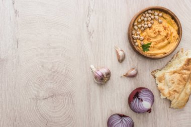 Lezzetli humus, taze pidenin yanında nohut, sarımsak ve bej ahşap masada kırmızı soğan.