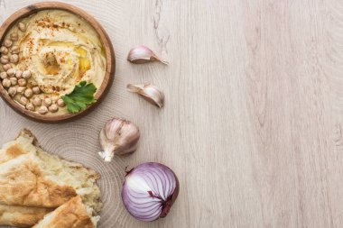 Lezzetli humus, taze pidenin yanında nohut, sarımsak ve bej ahşap masada kırmızı soğan.