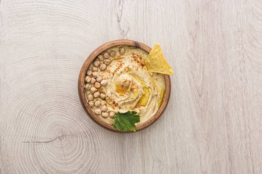 top view of delicious hummus with chickpeas and nacho in bowl on beige wooden table clipart