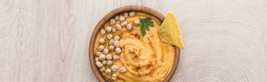 Bej ahşap masada nohut ve nacho ile nefis humus manzarası, panoramik çekim.