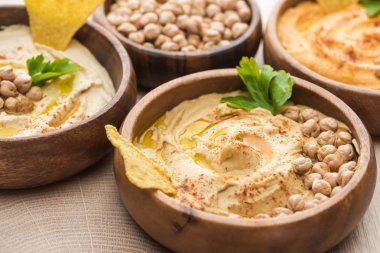 close up view of delicious hummus with chickpeas and nacho in bowls on beige wooden table clipart