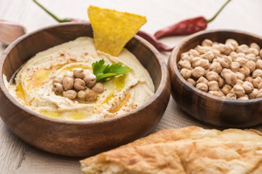 Bej ahşap masada taze pişmiş taze pidenin yanında bezelyeli enfes humus manzarası.
