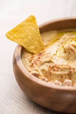 close up view of delicious hummus with nacho in bowl on beige wooden table clipart
