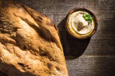 Tahta kırsal masada taze pişmiş pidenin yanında nefis humus manzarası.