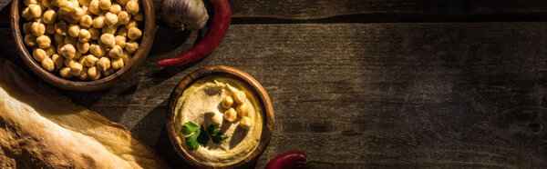 top view of delicious hummus, chickpeas, pita, spices on wooden rustic table, panoramic shot