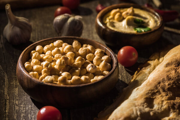 selective focus of delicious hummus, chickpeas, pita, vegetables and spices on wooden rustic table