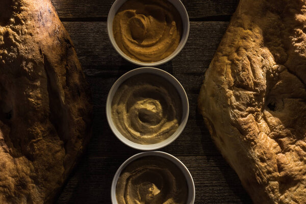 top view of delicious assorted hummus and fresh baked pitas on wooden rustic table