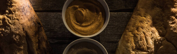 top view of delicious assorted hummus and fresh baked pitas on wooden rustic table, panoramic shot