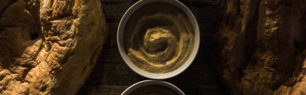 top view of delicious assorted hummus and fresh baked pitas on wooden rustic table, panoramic shot