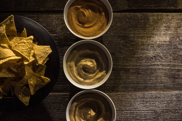top view of delicious assorted hummus with corn nachos on wooden rustic table