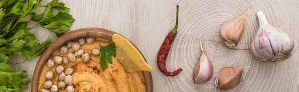 ひよこ豆とおいしいフムスのトップビュー ベージュの木のテーブルのスパイスとパセリの近くのボウルにナチョ パノラマショット — ストック写真