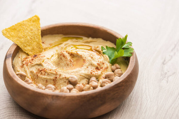 close up view of delicious hummus with chickpeas and nacho in bowl on beige wooden table