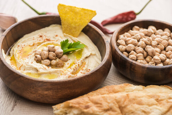 close up view of delicious hummus with chickpeas in bowl near fresh baked pita on beige wooden table
