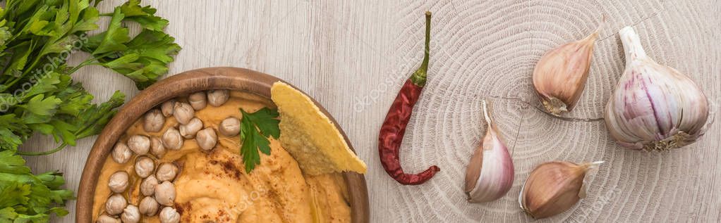 Top view of delicious hummus with chickpeas, nacho in bowl near spices and parsley on beige wooden table, panoramic shot — Stock Image Top View Delicious Hummus Chickpeas Nacho Bowl Spices Parsley Beige Stock Picture