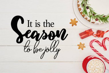 Beyaz ahşap masa üzerindeki kremalı Noel pastasının en üst görüntüsü şeker kamışları, hediyeler ve kakao ile birlikte neşeli harfler olma zamanıdır.