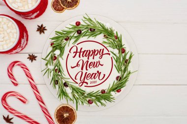 Çubuk şeker, iki fincan kakao ve beyaz ahşap masa üzerindeki kremalı noel pastası ve mutlu yeni yıl harfleri.