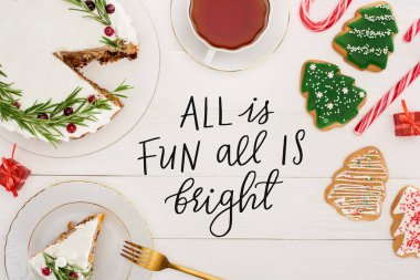 top view of christmas pie with rosemary, cup of tea and christmas tree cookies on white wooden table with all is fun all is bright illustration clipart
