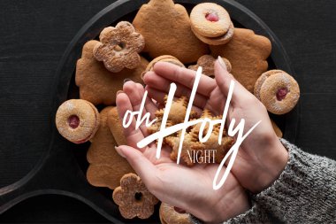 partial view of woman holding snowflake cookies in hands with o holy night lettering clipart