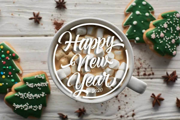 top view of Christmas cacao with marshmallow in mug on white wooden table near anise and cookies with happy new year lettering