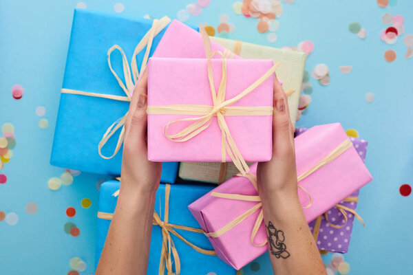 обрезанный вид женщины, держащей розовую подарочную коробку рядом красочные подарки рядом конфетти на синий
 