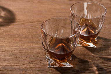 Two glasses of brandy with shadow on wooden table clipart