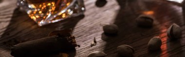 Glass of brandy with cigar and pistachios on wooden table, panoramic shot clipart