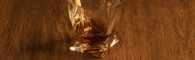 Panoramic shot of brandy in glass on wooden table clipart
