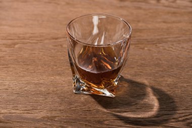 Glass of brandy with shadow on wooden table clipart