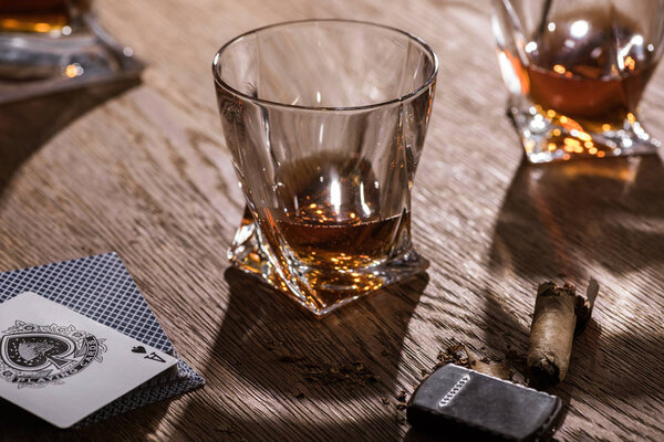 KYIV, UKRAINE - NOVEMBER 7, 2019: Glasses of brandy with cigar, lighter and playing cards on wooden table