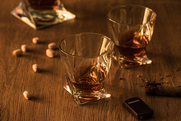 Glasses of brandy with pistachios, cigar and lighter on wooden table