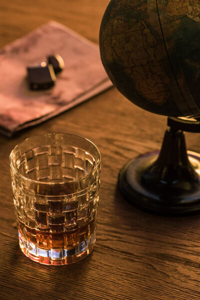 Glass of brandy with globe and lighter on map on wooden table