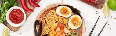 Taze malzemelerin yanında baharatlı deniz mahsulü ramen ve beyaz yüzeyde çubuk, panoramik çekim.