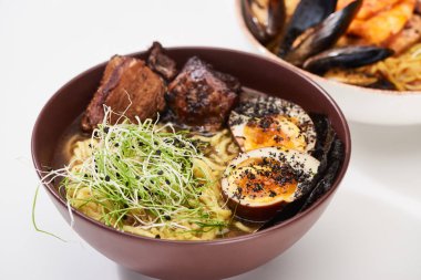 Beyaz yüzey üzerinde baharatlı deniz ürünleri ve et ramenlerinin seçici odağı.