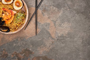 Taş yüzeyinde çubukları olan baharatlı deniz mahsulü ramen manzarası.