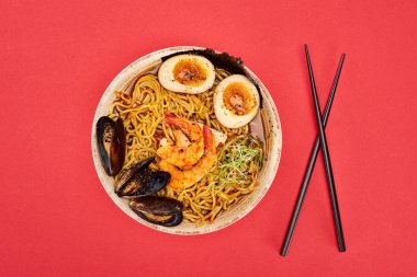 Kırmızı üzerine izole edilmiş çubukların yanında baharatlı deniz mahsulleri ramen manzarası.
