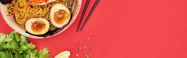 Yemek çubuklarının yanında baharatlı deniz mahsulleri ramen, maydanoz ve limon kırmızı panoramik karede izole edilmiş.
