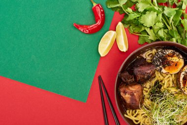 Taze malzemelerin yanında baharatlı ramen ve yeşil ve kırmızı yüzey üzerinde çubuklar.